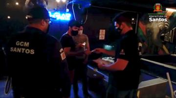 dois guardas municipais entregam documento para dois homens dentro de bar. #paratodosverem