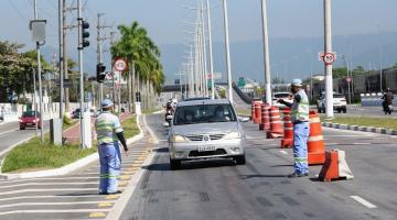 Dois agentes da CET em cada lado de uma vista de veículos. Uma fila de carros está formada e passando ao lado de cones. #paratodosverem