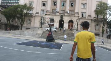 Jovem observa quadra de basquete 3x3 em frente a Prefeitura #paratodosverem