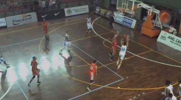 Jogador vestido de uniforme branco arremessa bola marcado por jogador de vermelho e outros atletas em volta. na quadra de basquete. #pratodosverem