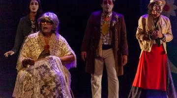 quatro peços em um cenário teatral. Uma delas é uma senhora, que está sentada. Atrás, mais três pessoas. #paratodosverem 