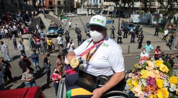 Beth em cima do carro do Corpo de Bombeiros exibe medalha com várias pessoas ao fundo. #paratodosverem