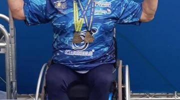 Atleta ergue braços com medalhas em pódio de primeiro lugar #paratodosverem