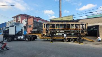Antigo bonde é transportado de galpão por carreta. #paratodosverem