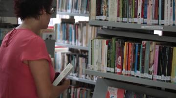 Mulher observa livros na prateleira #paratodosverem
