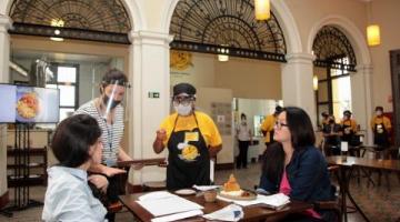 Duas mulheres, sentadas, são atendidas no Restaurante-Escola. #pracegover