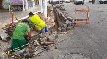 Homens trabalham na construção de bocas-de-lobo na via. #paratodosverem