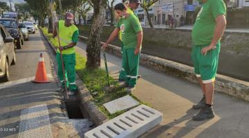 Operários preparam instalação de cobertura de boca de lobo em concreto. Eles estão em uma calçada ao lado de um canal. #paratodosverem