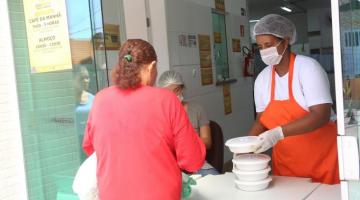 Mulher entrega marmita para outra mulher de costas. #paratodosverem