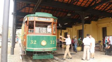 o bonde turístico está parado na estação. Há movimento de pessoas no entorno. #paratodosverem