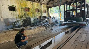 operários olham bonde em garagem #paratodosverem
