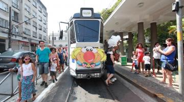 Bonde colorido no trilho e vários pais e crianças ao lado #paratodosverem