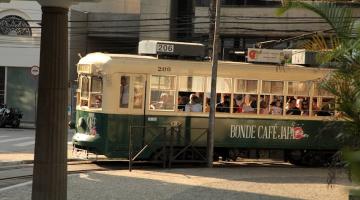 bonde fazendo curva em esquina do centro de santos. Na lateral do veículo está escrito Bonde Café Japão. #paratodosverem