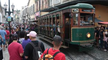 bonde circula em rua com grande público em torno. #paratodosverem 