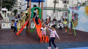 crianças estão subindo na escada e descendo o escorregador. Elas se divertem. Ao fundo, outras crianças estão brincando nos balancês. #paratodosverem