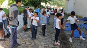 crianças uniformizadas estão se divertindo ao ar livre. Há colchonetes pelo chão. #paratodosverem