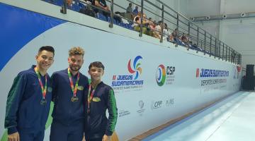 Kevin Medziu, Felipe Werle e Erik Medziu posam para a foto com medalhas no peito. #paratodosverem