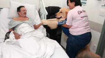 mulher pega cão no colo e o aproxima de paciente deitado #paratodosverem