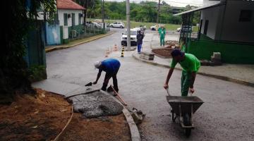 homens passam concreto em trecho de calçada. Um deles aplica a massa. O outro está segurando um carrinho de mão. #paratodosverem 