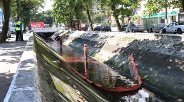 Canal com mancha vermelha. Há uma barreira instalada e dois homens dentro do canal. #paratodosverem