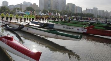 CANOAS HAVAIANAS VAZIAS ESTÃO PARADAS NA BEIRA DO MAR. aO FUNDO, EQUIPES UNIFORMIZADAS. #PARATODOSVEREM