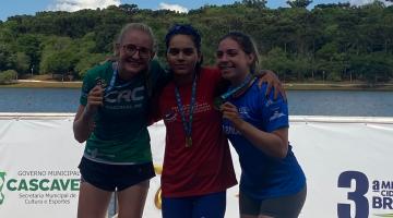 três atletas exibem medalhas com rio ao fundo #paratodosverem