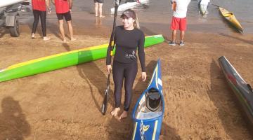 bruna posa para foto em beira de rio, ao lado da canoa. #paratodosverem