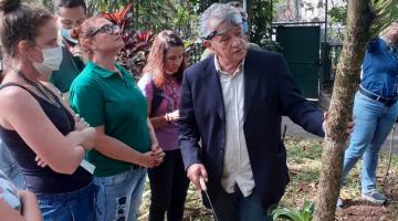 homem está apontando para árvore em área de vegetação. Pessoas em volta estão olhando. #paratodosverem