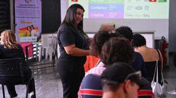 mulher em pé dá aula para pessoas em sala. #paratodosverem
