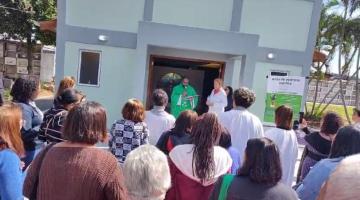 pessoas em pé diante de capela assistem padre falando ao fundo. #paratodosverem 