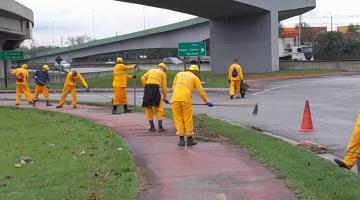 homens uniformizados capinam canteiro em avenida. #paratodosverem 
