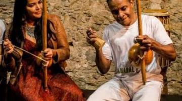 Duas pessoas trocam instrumentos em roda de capoeira #paratodosverem