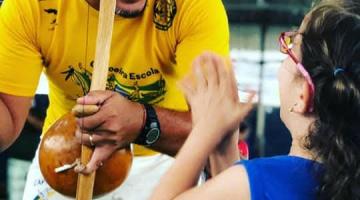 mestre toca berimbau diante de criança. #paratodosverem
