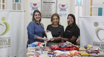 representantes do shopping e do fundo seguram alimento atrás de mesa cheia de alimentos #paratodosverem