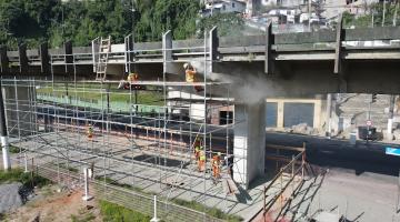 andaime na lateral de elevado, com homens trabalhando junto à estrutura. #paratodosverem