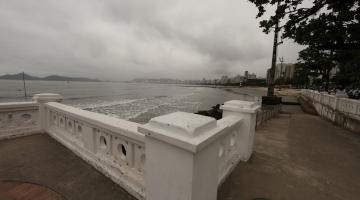 vista da faixa marítima a partir de mureta em primeiro plano na ponta da praia. O dia está nublado e o mar está calmo, com maré baixa. #paratodosverem 