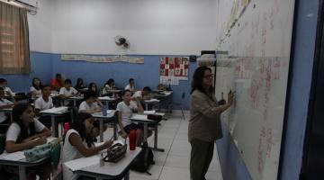 professora escreve no quadro e estudantes olham em sala de aula #paratodosverem