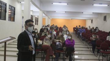 Homem em primeiro plano dando palestra e atrás mulheres sentadas em cadeiras. #paratodosverem