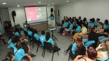 auditório com pessoas sentadas e uma delas em pé e falando à frente de um telão. #paratodosverem 