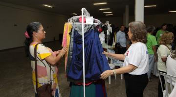 duas mulheres estão mexendo em roupas penduradas em arara num saguão. #paratodosverem 