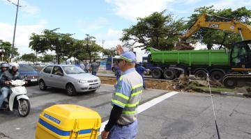 agente de trânsito está sinalizando para veículos. Ao fundo, no canteiro central há um caminhão e uma escavadeira. #paratodosverem