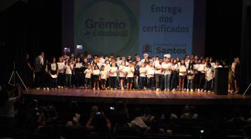 crianças seguram diploma em palco. #paratodosverem