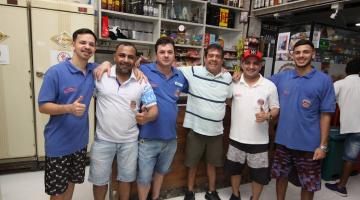 Homens abraçados em frente a balcão de restaurante. #paratodosverem