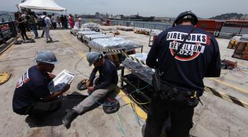 homens estão trabalhando ao lado de estruturas com fogos em uma balsa. #paratodosverem 