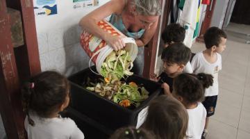 crianças observam mulher despejar em composteira #paratodosverem