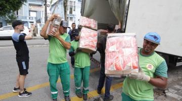 homens carregam caixas com pacotes de frango. há um caminhão atrás com a porta aberta, de onde eles retiram as caixas. #paratodosverem 