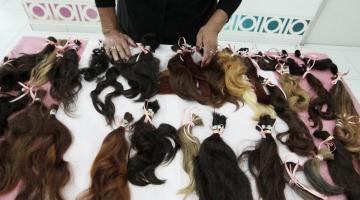 várias mechas de cabelo dispostas sobre uma mesa. Ao fundo aparecem as mãos de uma mulher. #paratodosverem 