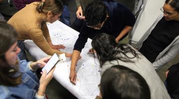 pessoas observam mapa sobre uma mesa. #paratodosverem
