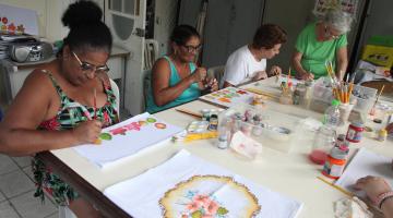 mulheres pintam panos de prato sobre uma mesa. #paratodosverem
