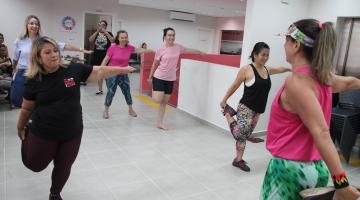 mulheres fazem alongamento com as pernas em salão. #paratodosverem 